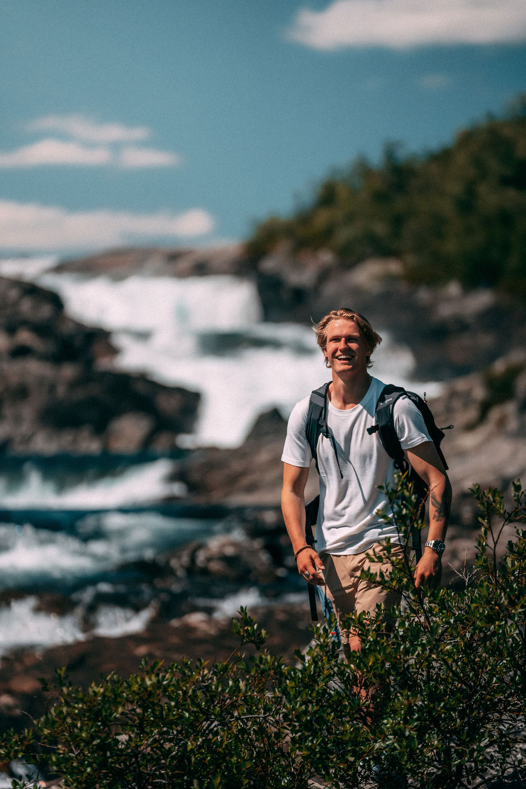 Smilende mann med ryggsekk foran fossende elv