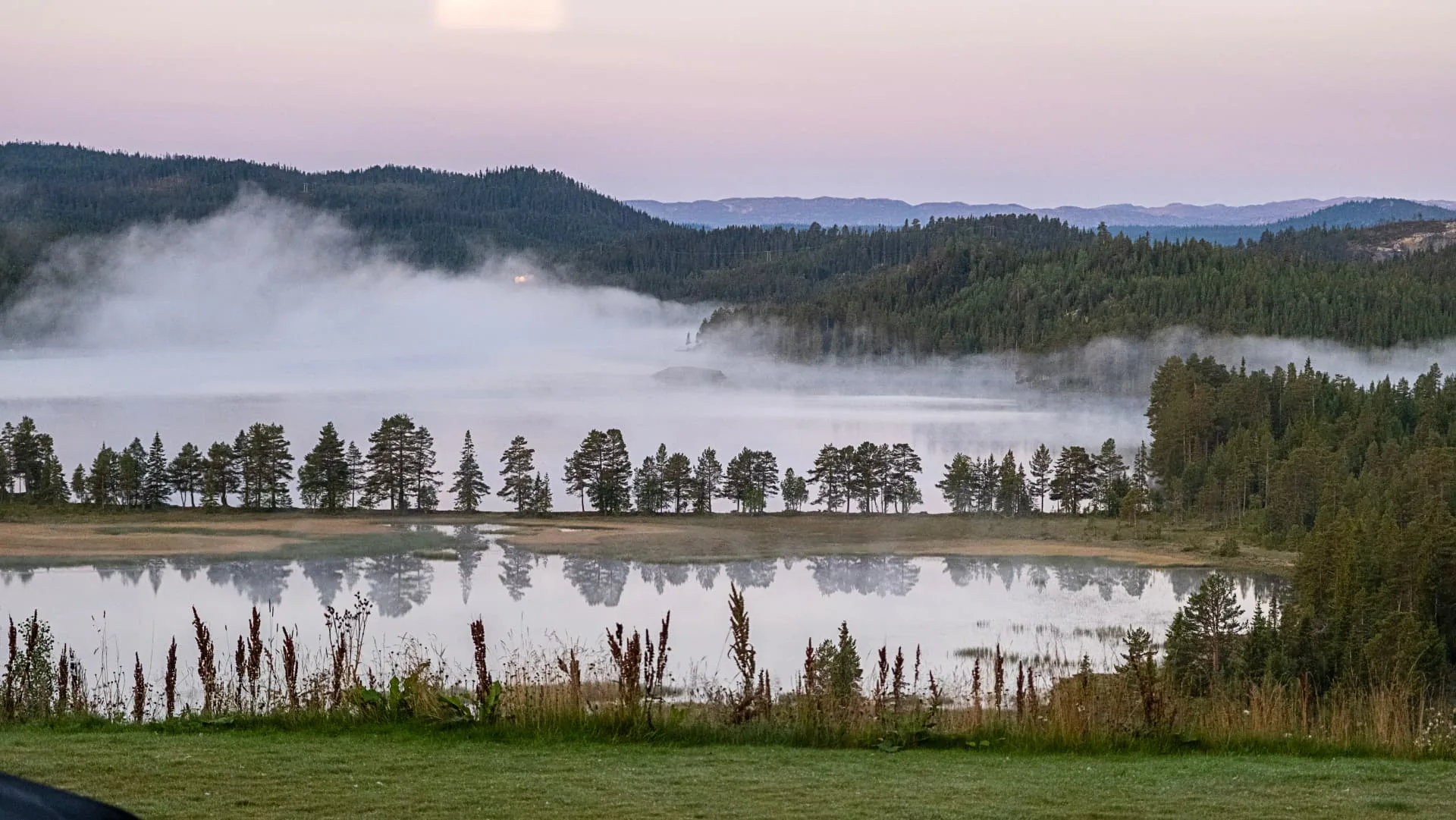 Tåke over stille fjellvann i morgengry nær Rauland