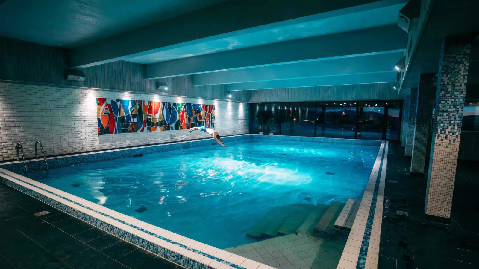Innendørs basseng på Rauland Høgfjellshotell med fargerikt mosaikk og svømmer