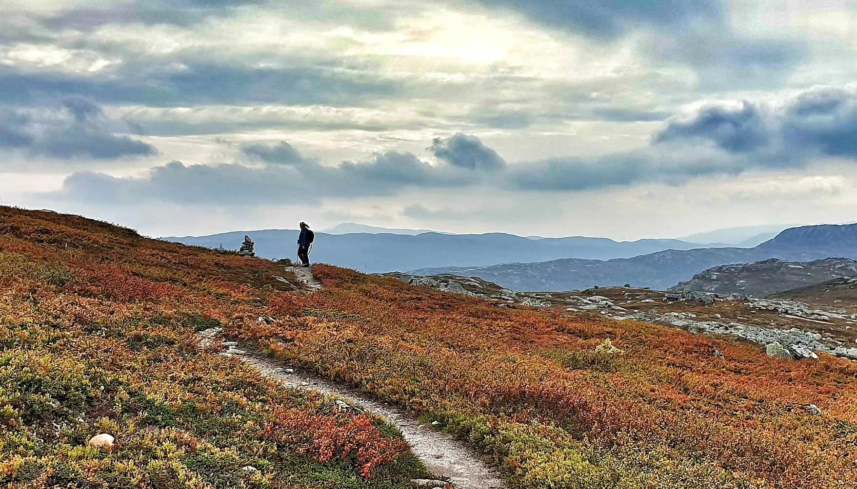 Silhuett av turgåer ved varde med skyer over Hardangervidda
